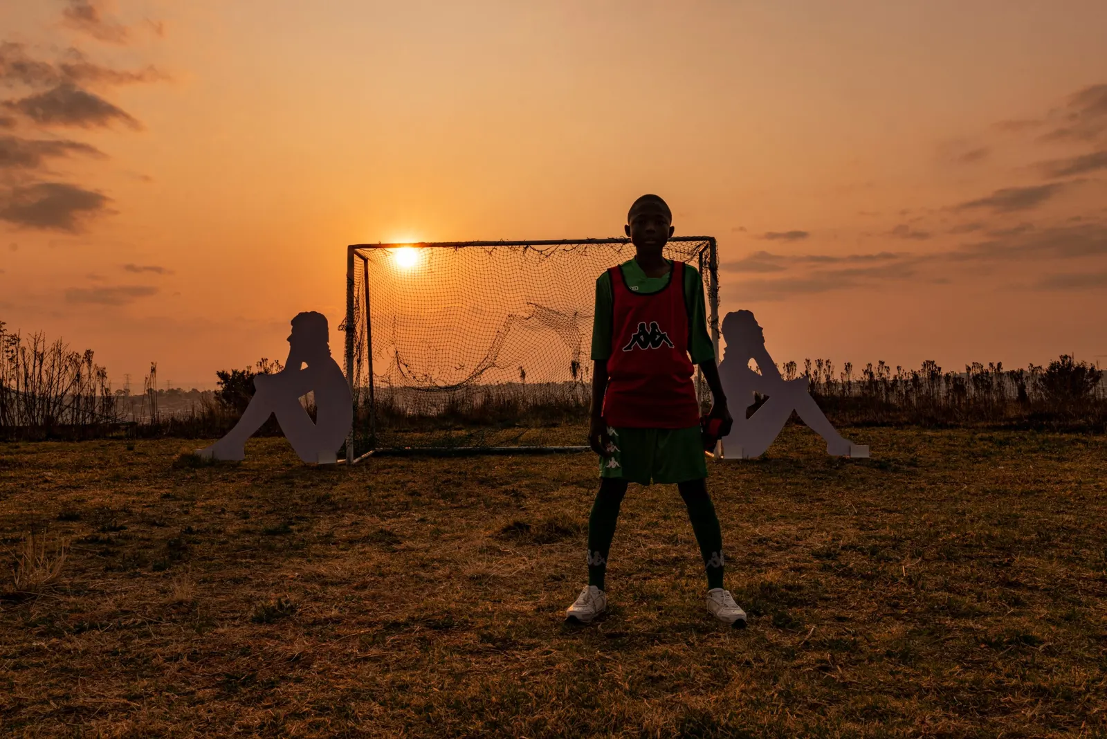 Young footballer silhouetted at sunset in front of goal, Kappa campaign